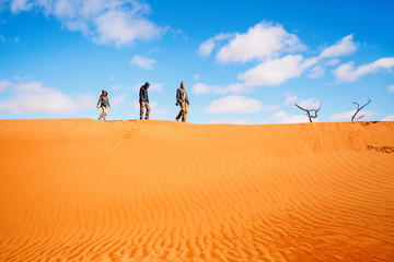 Family climbing up red sand dune