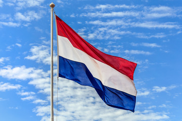 Fototapeta na wymiar The national flags of the Netherland flag on the background of blue sky with clouds.