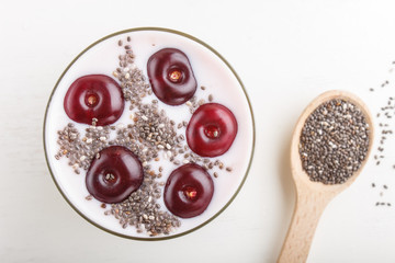 Yoghurt with cherries, chia seeds and granola in glass with wooden spoon on white wooden background. top view.