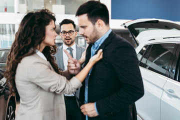 Angry married couple is discussing in a car sale salon or showroom