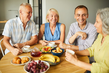 Group of mature people chatting cheerfully while sitting around table in kitchen, copy space