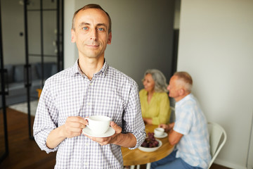 Waist up portrait of smiling mature man looking at camera posing at home with friends in...