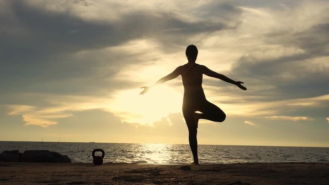 Full length rear view of the silhouette of a sporty while practicing yoga pose, shot at sunset during summer vacation video format 4k. health concept.