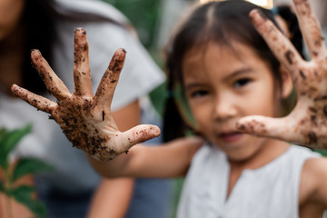 Asian child girl showing dirty hands after planting the tree in the garden