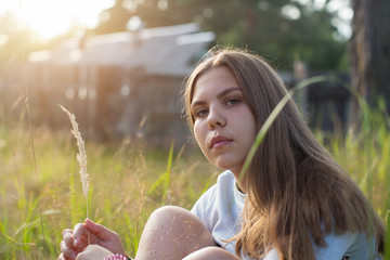 Pretty girl sitting in green grass in summer countryside.