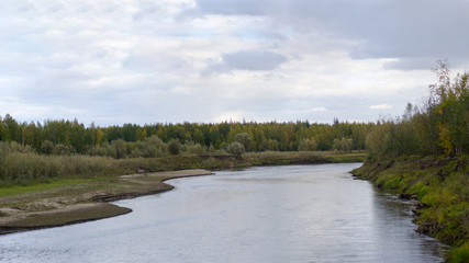 North kempendyay river to the shore of sand eroded by the flow of water in the spruce forest the tundra of Yakutia and puffy clouds in the afternoon.