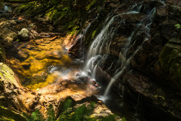 small beautiful waterfall in the forest rundown the rock face with sunlight shine on the rocky creek down below