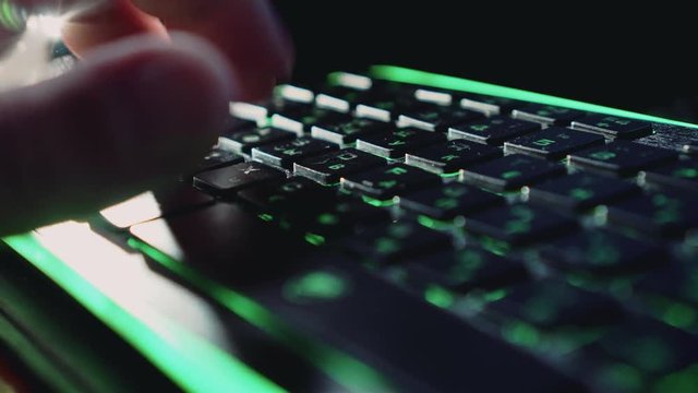 A man's hand vigorously prints on the keyboard with backlight. Nice lighting. Close up. Writer's job. Fast printing. Computer technology.