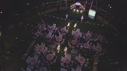 Drone flying over wedding dinner decoration, or marriage anniversary, in the garden outdoor, catering setting chairs and tables, aerial view. Tropical decor style atmosphere.