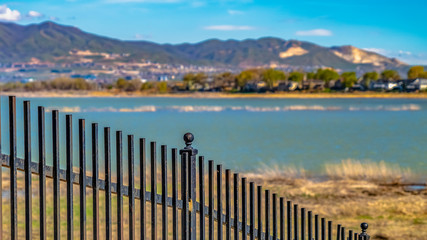 Panorama frame Black metal fence with a lake and grassy shore in the background