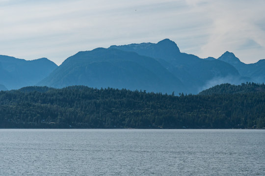 forest covered island over the horizon on a hazy day with smoke rise behind forest in front of the mountain range