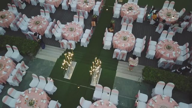 Drone flying over wedding dinner decoration, or marriage anniversary, in the garden outdoor, catering setting chairs and tables, aerial view. Tropical decor style atmosphere.