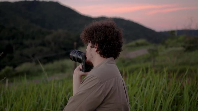 A young male photographer looks around at the setting while holding his camera during an outdoor portrait session.