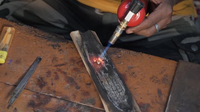 Industrial worker is in a fabric and uses forceps and burner to work out an element for jewelry
