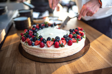 Chef hands cutting by knife delicious raspberry cake with fresh strawberries, raspberries, blueberry.