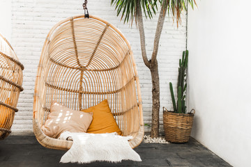 Wicker rattan hanging chair in loft cafe. Eco friendly furniture style and concept. Orange pillows...
