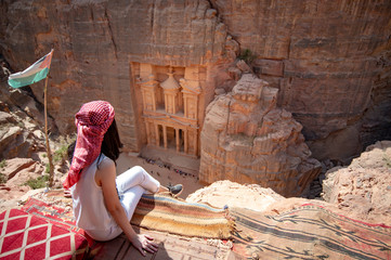 Asian woman traveler sitting on carpet viewpoint in Petra ancient city looking at the Treasury or...
