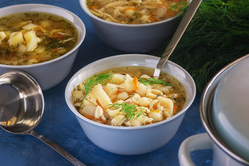 Chicken Noodle Vegetable Soup Spice with Herb. Full Bowl of Starter with Spoon. Hot Meat Bouillon with Pasta and Potato Elevated View. Pot and Ladle on Dark Table. Healthy Homemade Food