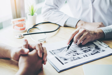 Dentist talking to male patient and presenting results on Dental x-ray film About the problem of the patient in dental office