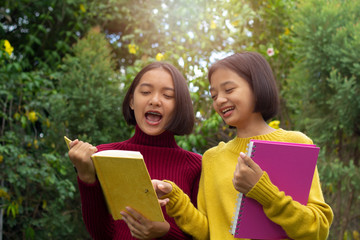 Two Asia young girl talking and hold note book with nature background.