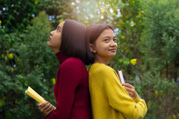 Two happy young Asian girls hold note book  with green background.
