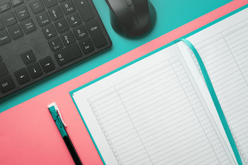 Top view notebook with a ballpoint pen and keyboard with a computer mouse on a colored background