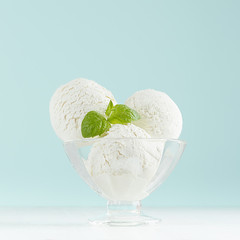 Delicious classic creamy ice cream scoops in  glass ice-cream bowl with green mint in modern mint color interior on white wood board, square, closeup.