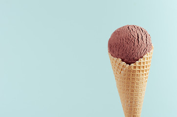 Chocolate brown creamy ice cream in crisp waffle cone on pastel green background, closeup, details, top, half.