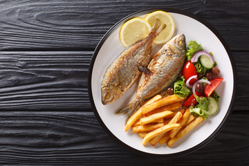 Traditional fried Sarpa salpa fish with lemon and side dish of fresh vegetable salad. french fries close-up on a plate. horizontal top view