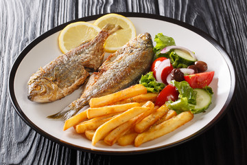 Adriatic fried Sarpa salpa fish with lemon served with fresh vegetable salad and french fries close-up on a plate. horizontal