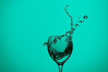 splash of water in wineglass isolated on green background.