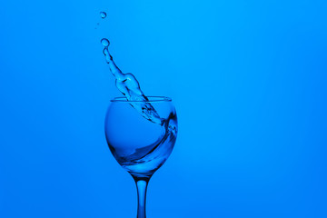 splash of water in wineglass isolated on blue background.
