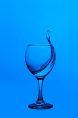splash of water in wineglass isolated on blue background.