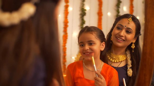 South Indian woman in traditional wear helping her daughter to get ready for the celebration of Diwali - lifestyle Family. Beautiful mother teaching her young daughter how to use a makeup brush - m...