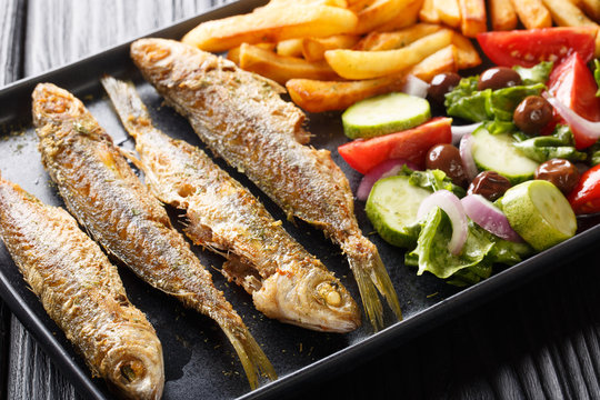 Fried boops boops fish with fresh vegetable salad and french fries close-up on a plate. horizontal