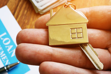 Hand is holding key from property and mortgage loan agreement.