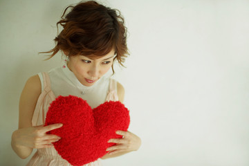 ハートのクッションを持って微笑む女性