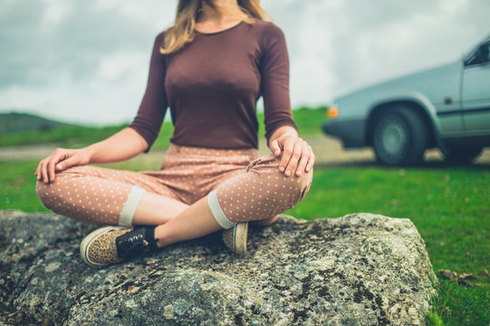 Young woman in meditation pose by her car