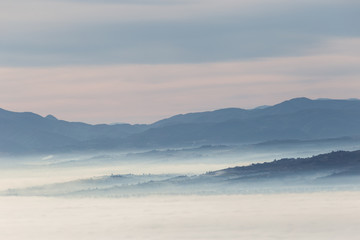 Fog filling a valley in Umbria (Italy) at dawn, with layers of mountains and hills and various shades of blue
