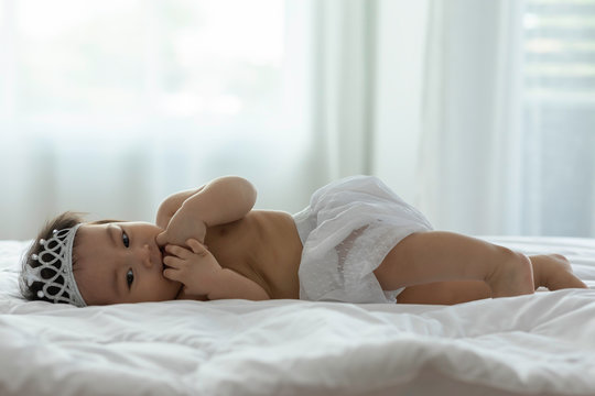 Cute Sweet Adorable Asian Baby wearing bride dress and diadem Sitting on white bed smiling and playing with happiness emotional in cozy bedroom,Healthy Baby Concept