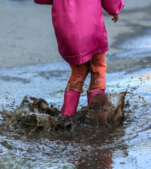 Playful child outdoor jump into puddle in boot after rain