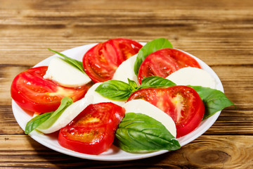 Italian caprese salad with tomatoes, mozzarella cheese and basil on a wooden table
