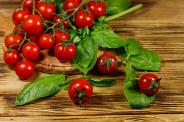 Fresh cherry tomatoes with green basil leaves on a wooden table