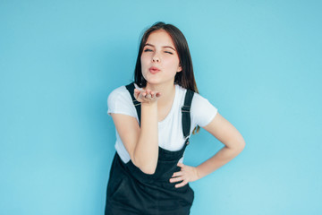 Beautiful carefree smiling girl with dark long hair in white t-shirt making air kiss isolated on blue background