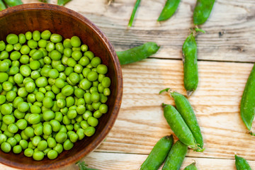 closeup green peas in brown dish, on wooden table.