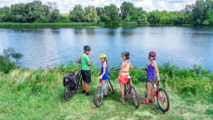 Family on bikes cycling outdoors, active parents and kids on bicycles, aerial top view of happy family with children relaxing near beautiful river from above, weekend and vacation sport and fitness co