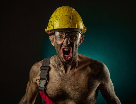 A man miner in a worker s clothes and a helmet, dirty, in soot, with a naked body, grimaces at the camera