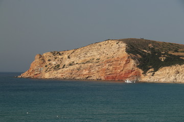 small boat next to red cliff on Milos