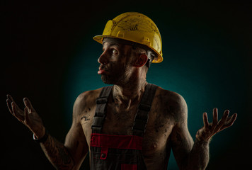 A man miner in a worker s clothes and a helmet, dirty, in soot, with a naked body, grimaces at the...