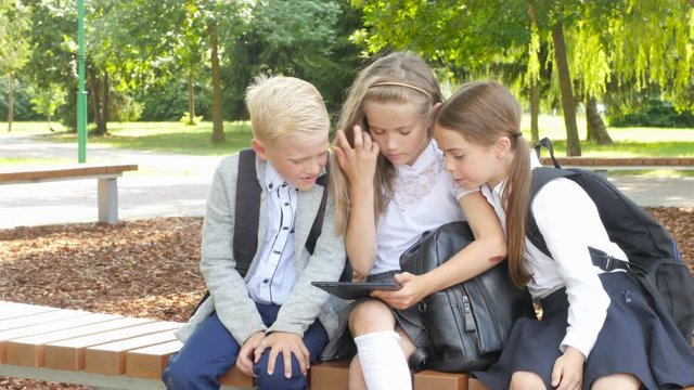schoolchildren in the park are sitting on a bench using a tablet to learn lessons. education. school students